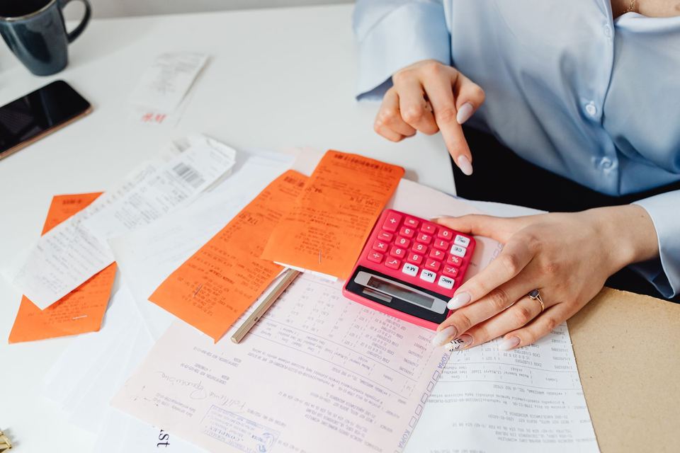 A person working through paper receipts with a calculator at a desk