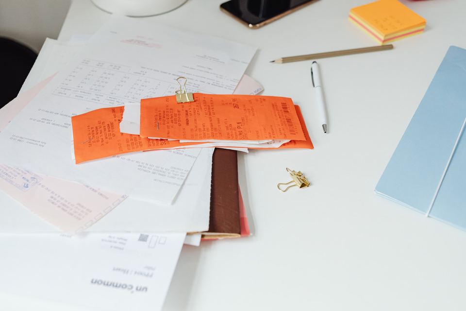 Till receipts clipped together on top of a pile of paperwork on a white desk