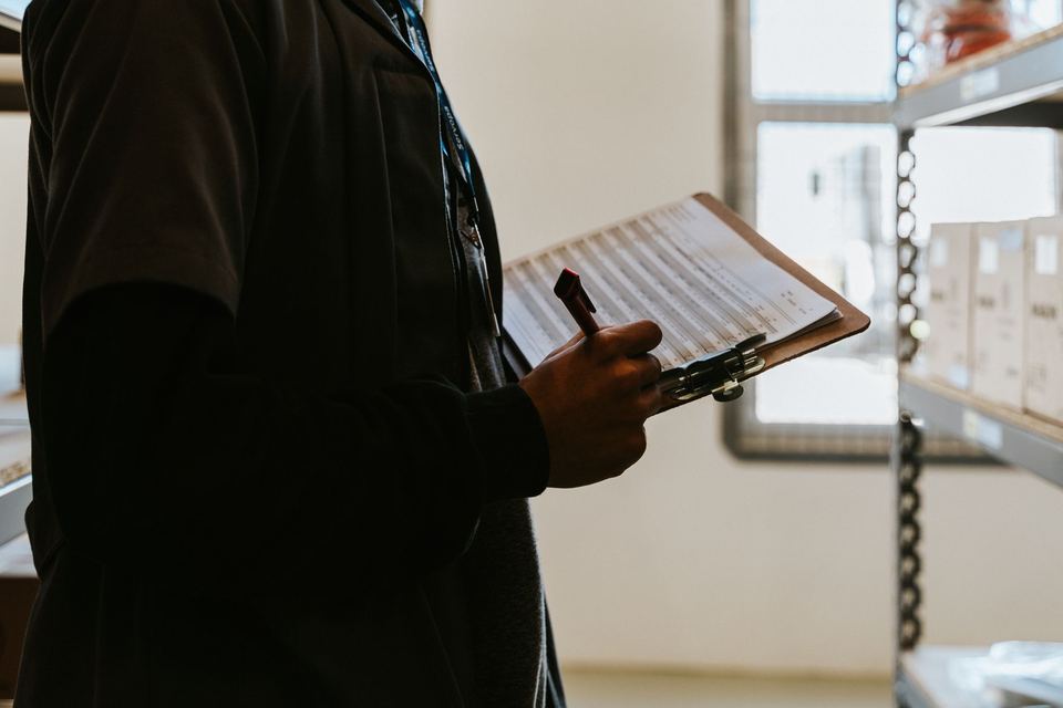 A person checking stock against a clipboard in a warehouse
