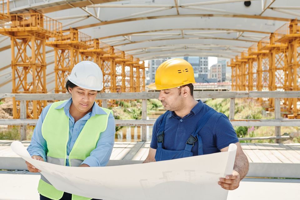 Two people in hard hats reading a large drawing on a building site