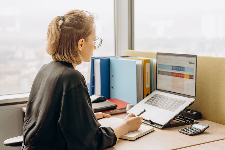 A woman working through a spreadsheet on a laptop, with box files beside her