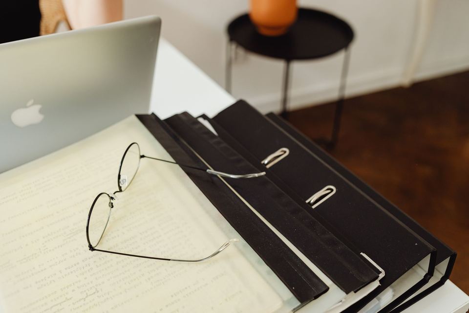 Lever arch files and a pair of glasses on a desk beside a laptop